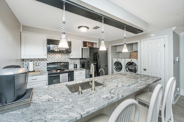 kitchen with white cabinets, washing machine and dryer, decorative light fixtures, and black appliances