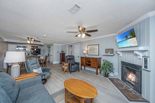 living room featuring ceiling fan, crown molding, light hardwood / wood-style flooring, and a fireplace