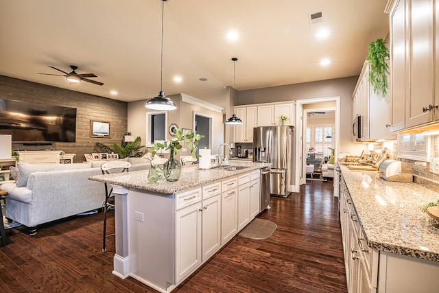 kitchen with appliances with stainless steel finishes, decorative light fixtures, an island with sink, and white cabinets