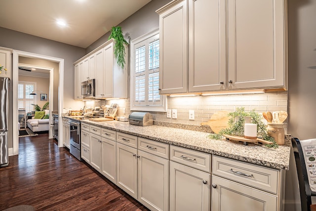 kitchen featuring light stone countertops, appliances with stainless steel finishes, white cabinets, decorative backsplash, and dark hardwood / wood-style floors