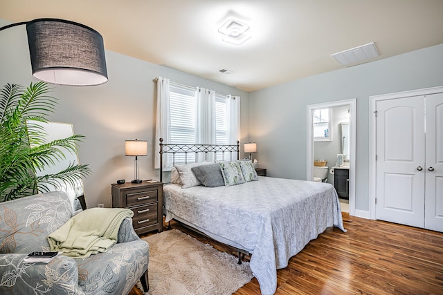 bedroom with multiple windows, ensuite bathroom, and dark hardwood / wood-style flooring