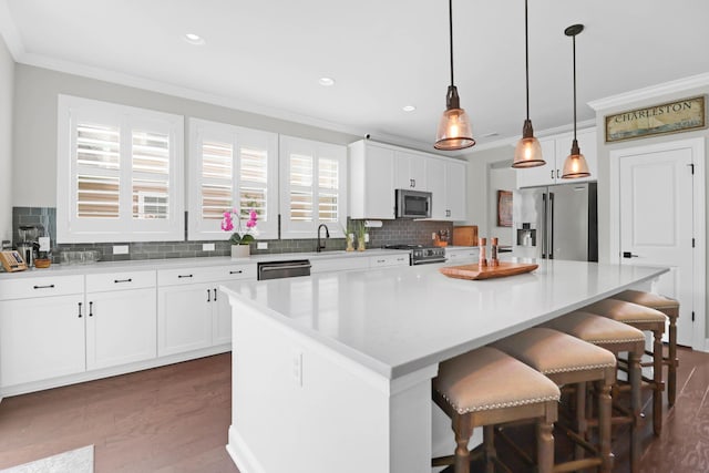 kitchen with crown molding, appliances with stainless steel finishes, white cabinets, a kitchen island, and decorative light fixtures