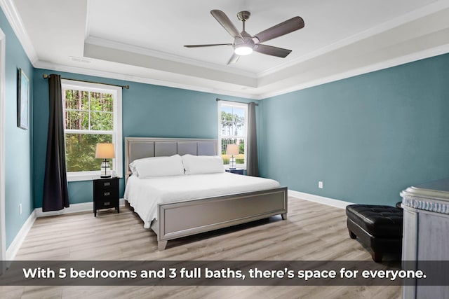 bedroom featuring ceiling fan, ornamental molding, a raised ceiling, and light wood-type flooring