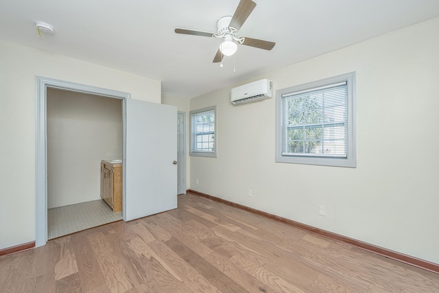 unfurnished bedroom with multiple windows, a wall mounted AC, light wood-type flooring, and ceiling fan