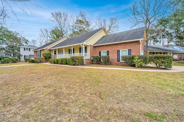 ranch-style home featuring covered porch, brick siding, a front lawn, and a shingled roof