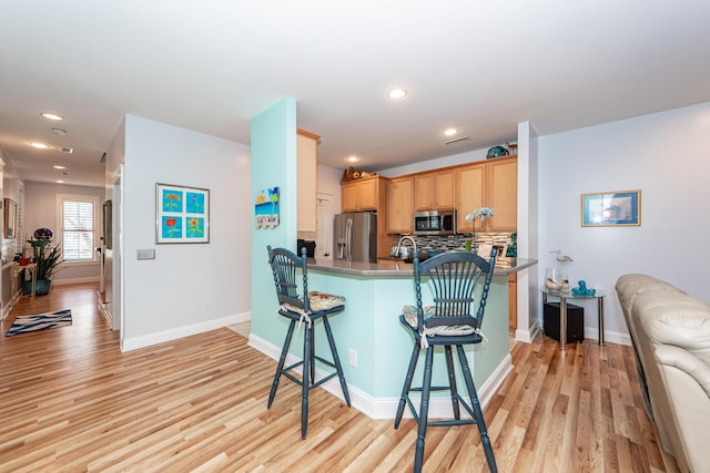 kitchen featuring backsplash, light hardwood / wood-style flooring, appliances with stainless steel finishes, kitchen peninsula, and a breakfast bar area