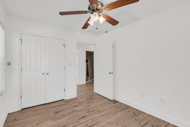 unfurnished bedroom with attic access, baseboards, ceiling fan, light wood-style flooring, and a closet