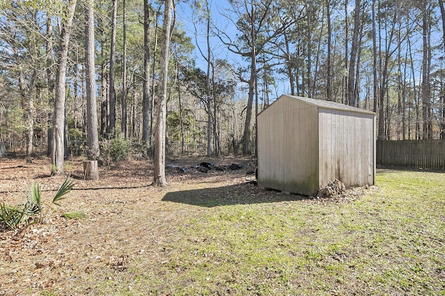 view of yard featuring a shed, fence, a view of trees, and an outbuilding