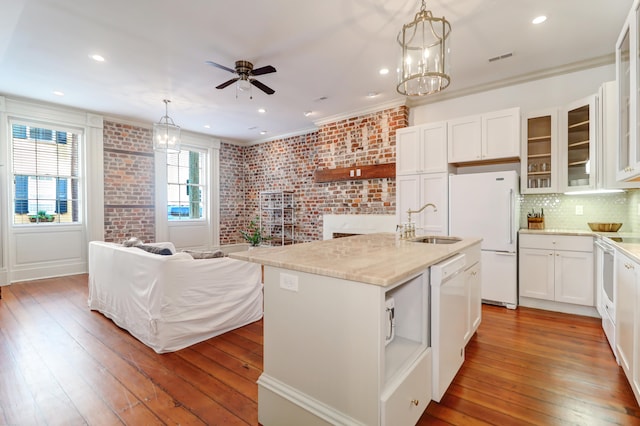 kitchen featuring brick wall, ceiling fan with notable chandelier, white appliances, an island with sink, and hardwood / wood-style flooring