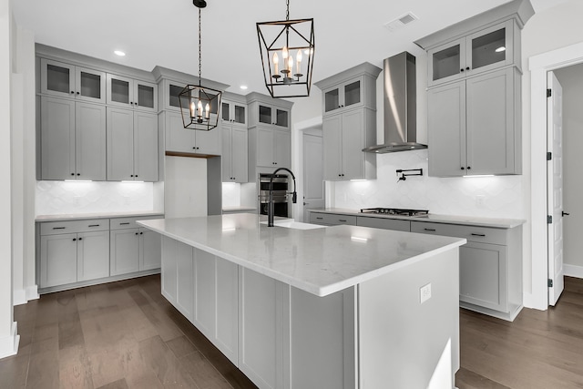 kitchen featuring stainless steel gas stovetop, dark hardwood / wood-style flooring, hanging light fixtures, a center island with sink, and wall chimney exhaust hood