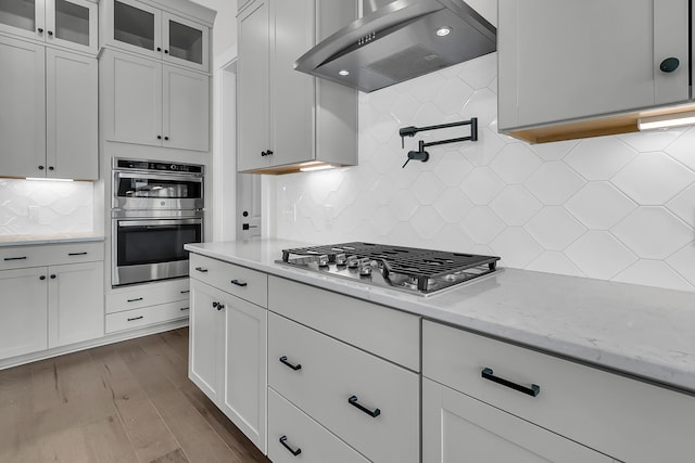 kitchen with white cabinetry, wall chimney exhaust hood, stainless steel appliances, and light stone counters