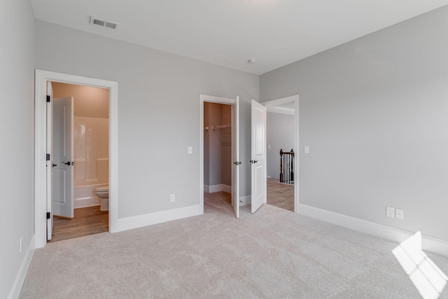 unfurnished bedroom featuring a walk in closet, ensuite bathroom, a closet, and light carpet