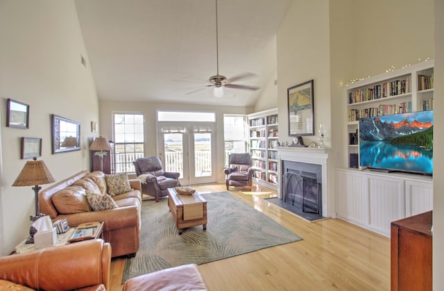 living room with built in shelves, ceiling fan, light hardwood / wood-style flooring, and high vaulted ceiling