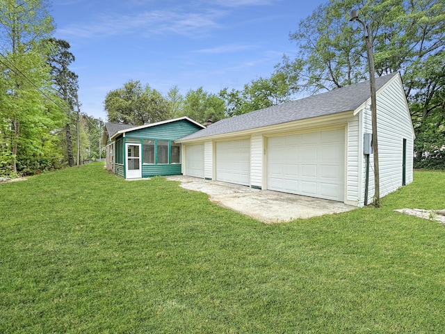 view of front facade featuring a front yard, a shingled roof, a sunroom, a detached garage, and an outbuilding