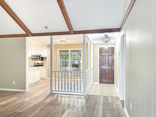 interior space with lofted ceiling with beams, wooden walls, visible vents, light wood finished floors, and baseboards