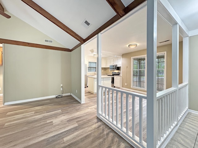 unfurnished room featuring light wood-type flooring, baseboards, vaulted ceiling with beams, and visible vents