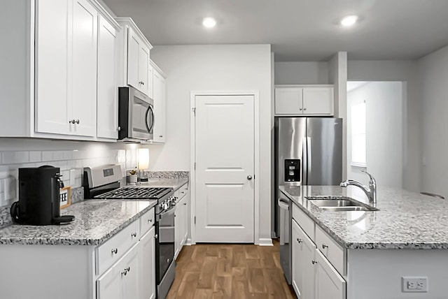 kitchen with an island with sink, stainless steel appliances, wood finished floors, white cabinetry, and a sink