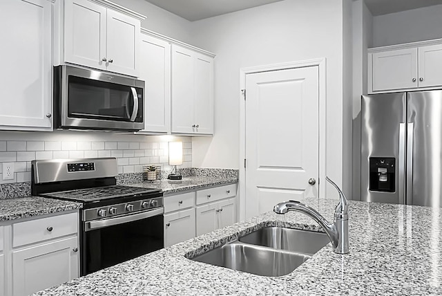 kitchen featuring a sink, light stone counters, tasteful backsplash, stainless steel appliances, and white cabinets