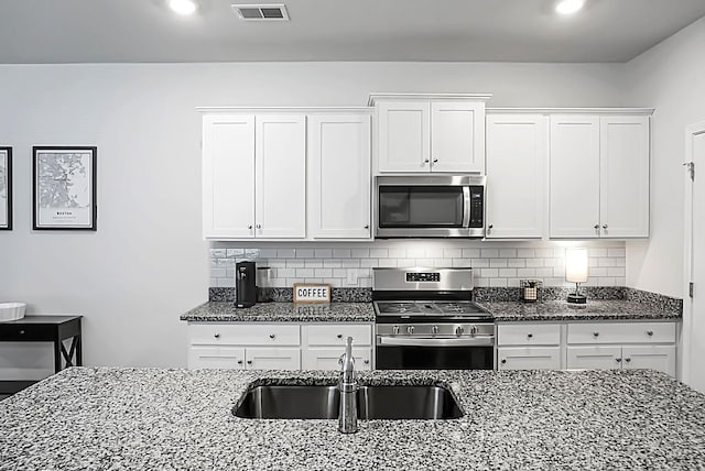 kitchen featuring decorative backsplash, dark stone counters, appliances with stainless steel finishes, and a sink