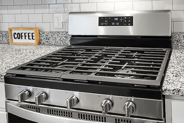 interior details featuring decorative backsplash, gas range, white cabinets, and light countertops