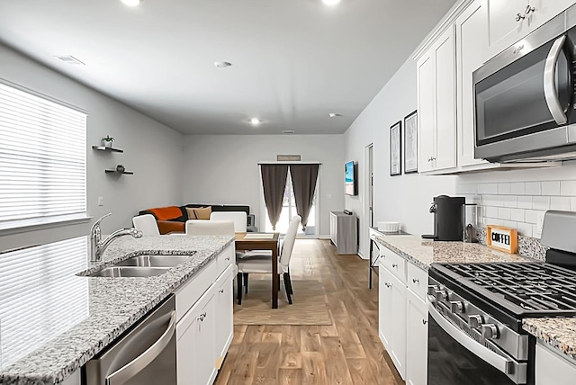 kitchen featuring light wood-type flooring, a sink, stainless steel appliances, white cabinetry, and tasteful backsplash