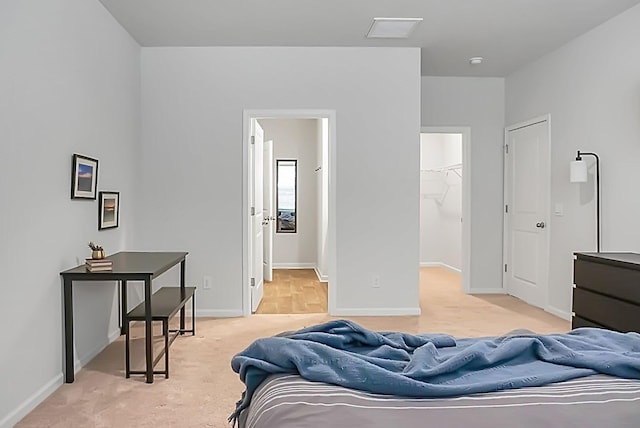 bedroom featuring light carpet, a closet, a walk in closet, and baseboards