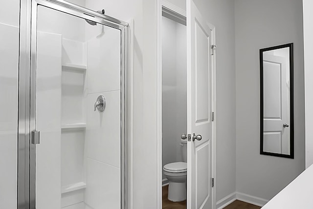 bathroom with a stall shower, toilet, baseboards, and wood finished floors