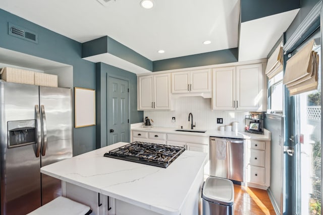 kitchen featuring a center island, sink, white cabinetry, light stone countertops, and stainless steel appliances