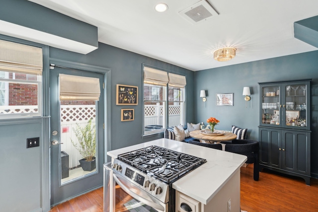 kitchen with stainless steel gas stove, light stone counters, and hardwood / wood-style flooring