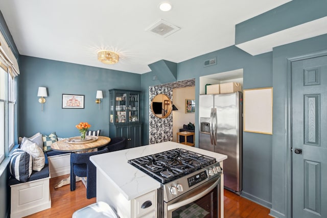 kitchen with light stone counters, hardwood / wood-style floors, appliances with stainless steel finishes, and a center island