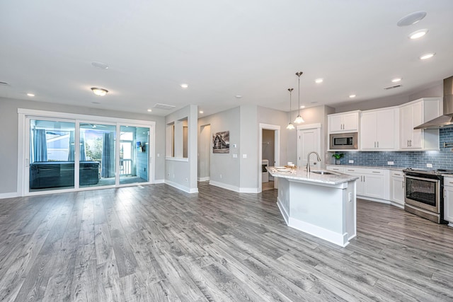 kitchen featuring a kitchen island with sink, white cabinets, hanging light fixtures, light wood-type flooring, and appliances with stainless steel finishes