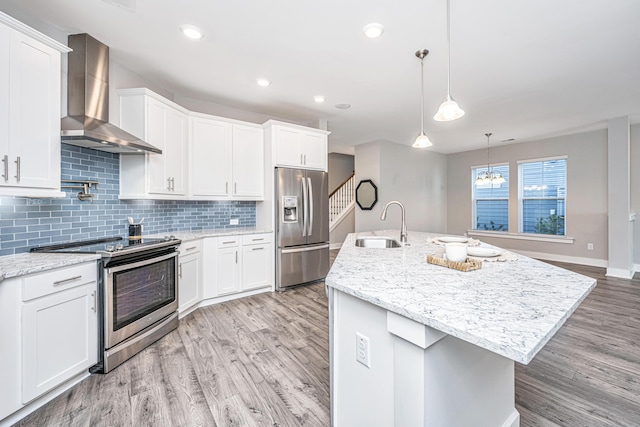 kitchen with wall chimney exhaust hood, pendant lighting, a center island with sink, white cabinets, and appliances with stainless steel finishes