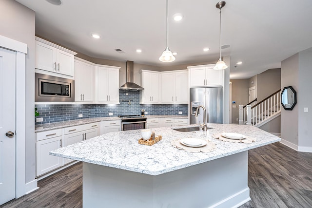 kitchen featuring a kitchen island with sink, sink, wall chimney exhaust hood, white cabinetry, and stainless steel appliances