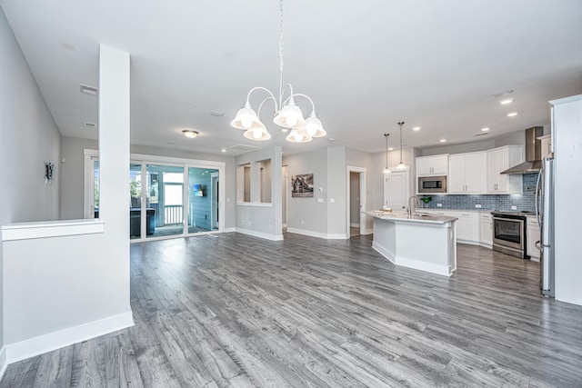 kitchen featuring pendant lighting, a kitchen island with sink, wall chimney range hood, white cabinetry, and stainless steel appliances