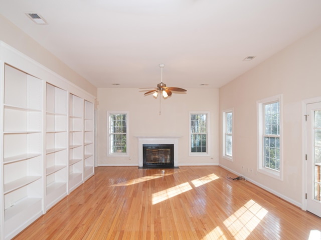 unfurnished living room with built in features, light hardwood / wood-style flooring, ceiling fan, and a healthy amount of sunlight