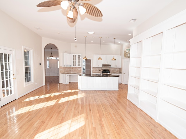 kitchen featuring backsplash, a kitchen island with sink, white cabinets, ceiling fan, and decorative light fixtures