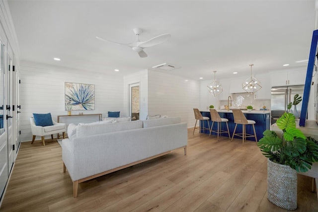 living area featuring recessed lighting, light wood-style flooring, and ceiling fan with notable chandelier