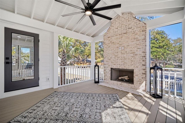 exterior space with lofted ceiling with beams, a brick fireplace, ceiling fan, and a wealth of natural light