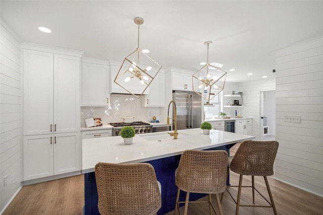 kitchen featuring high quality fridge, white cabinetry, light countertops, a center island with sink, and pendant lighting