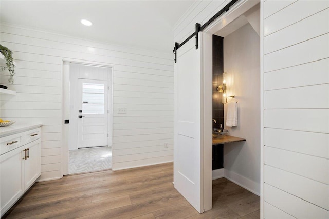 hall with light wood-style floors, a barn door, and recessed lighting