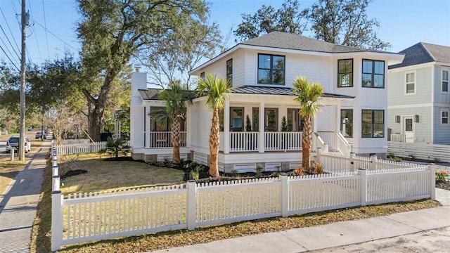 view of front of house featuring metal roof, a porch, a fenced front yard, a shingled roof, and a standing seam roof