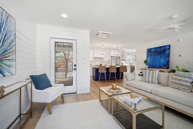 living area with ornamental molding, wood walls, light wood finished floors, and ceiling fan with notable chandelier