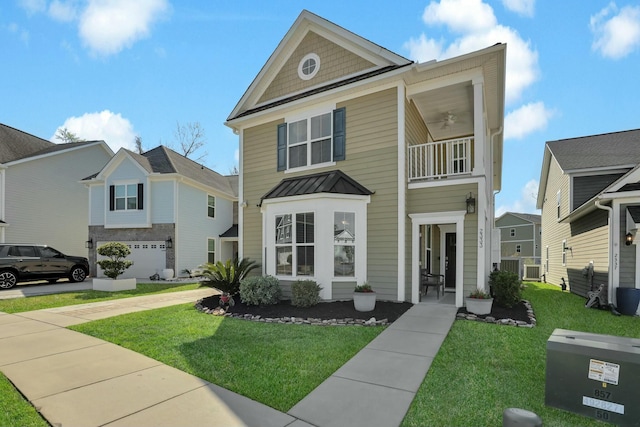 view of front of house with a front yard, a balcony, a ceiling fan, a standing seam roof, and metal roof