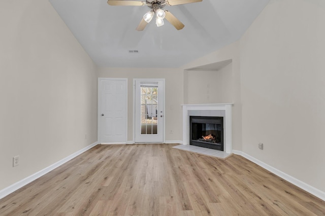 unfurnished living room with ceiling fan, a tiled fireplace, vaulted ceiling, and light hardwood / wood-style flooring