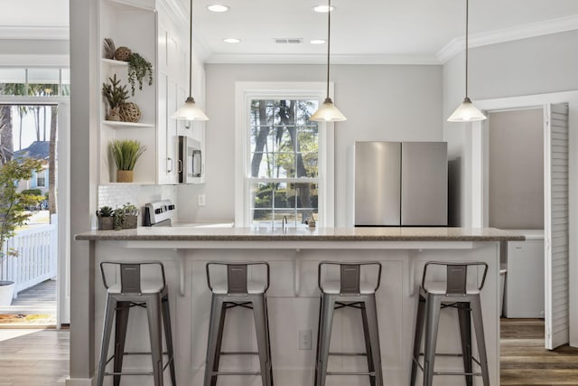 kitchen with dark hardwood / wood-style floors, tasteful backsplash, ornamental molding, appliances with stainless steel finishes, and decorative light fixtures