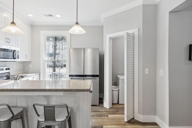 kitchen featuring appliances with stainless steel finishes, hanging light fixtures, decorative backsplash, and white cabinetry