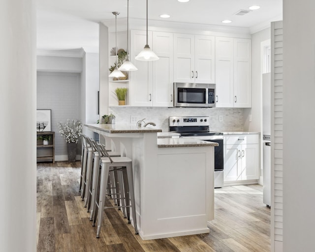 kitchen featuring wood-type flooring, a kitchen breakfast bar, light stone counters, stainless steel appliances, and white cabinets