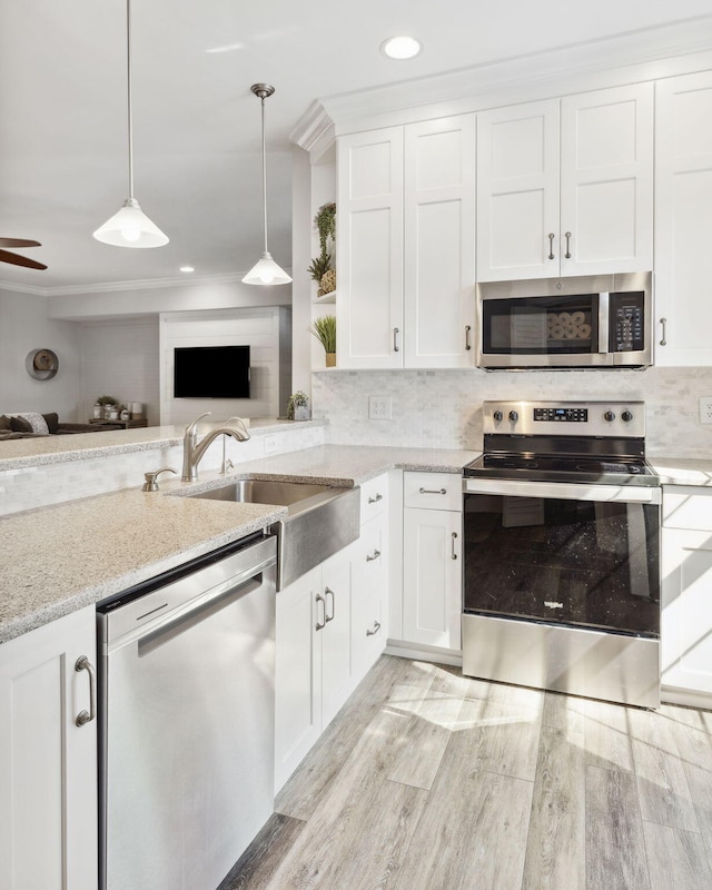 kitchen with white cabinets, appliances with stainless steel finishes, pendant lighting, and light hardwood / wood-style floors