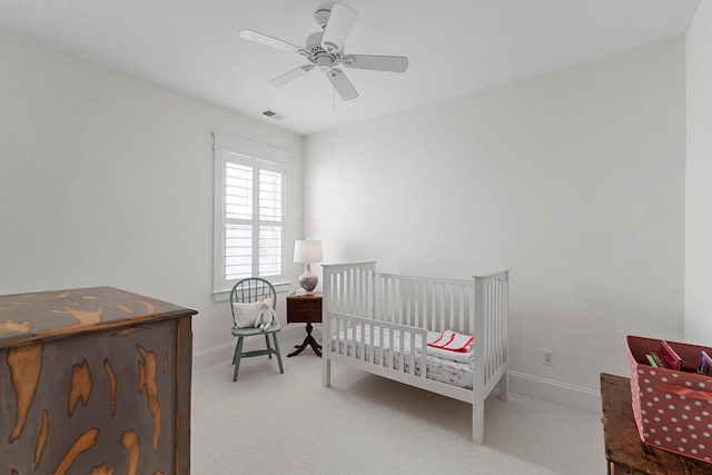 carpeted bedroom featuring a crib and ceiling fan