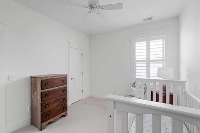 bedroom featuring light carpet, a nursery area, and ceiling fan